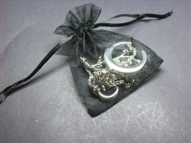 May include: A silver crescent moon pendant necklace and chain inside a small black mesh drawstring bag. The necklace is a delicate piece of jewelry, perfect for everyday wear or special occasions. The bag is closed with a black satin drawstring.