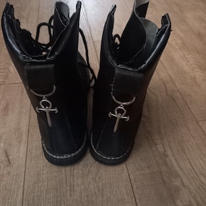 May include: A pair of black leather boots with silver ankh charms. The boots have laces and a chunky sole.