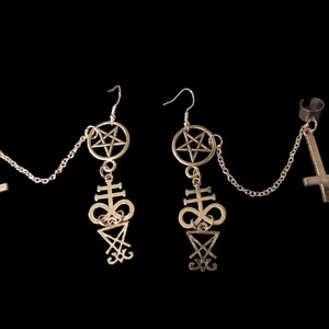 May include: A pair of gold-toned earrings with a pentagram, a cross, and a symbol of the Leviathan. The earrings are connected by a chain.