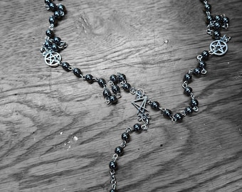 May include: A beaded necklace featuring dark metallic spherical beads linked by silver-toned metal chains. The necklace includes several circular silver-toned pentagram charms and a central silver-toned pendant depicting a winged figure.