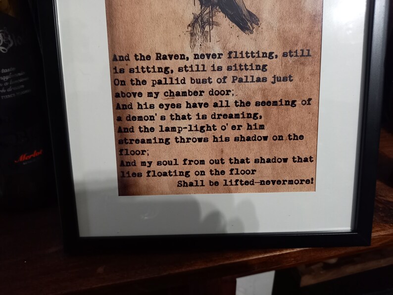 May include: Framed print featuring a poem with a raven illustration. The text, in a vintage typewriter font, includes the lines "And the Raven, never flitting...Shall be lifted-nevermore!" The print is in a black frame.