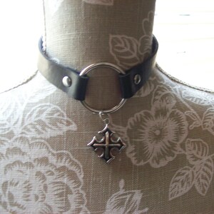 May include: A black leather choker with a silver ring and a silver cross pendant.