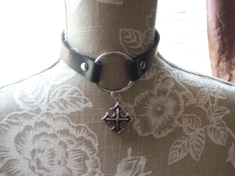May include: A black leather choker with a silver ring and a silver cross pendant.