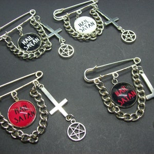 May include: Four silver safety pin brooches with a chain, a cross, and a pentagram charm. Each brooch features a round black and white or red and black button with the text "Hail Satan".