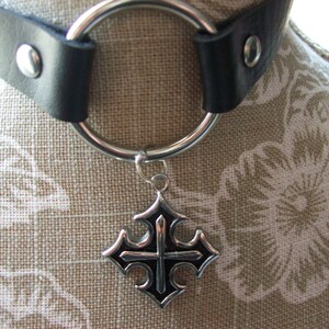 May include: A black leather choker with a silver ring and a silver cross pendant. The cross has a black center.