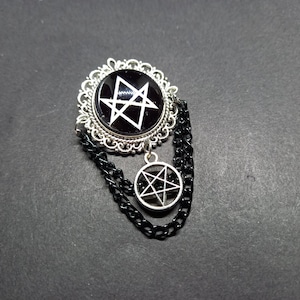 May include: A silver pendant with a black pentagram charm and a silver chain. The pentagram is surrounded by a silver filigree frame.
