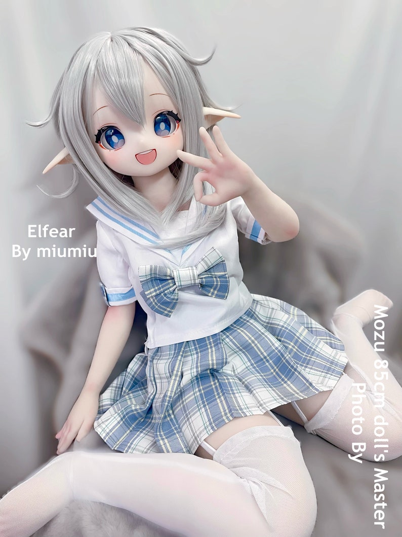 May include: A white doll with blue eyes and long silver hair wearing a white and blue sailor uniform with a plaid skirt and white thigh-high stockings. The doll is sitting on a white surface. The text "Elfear By miumiu" is visible in the image. The text "Mozu 85cm doll's Master Photo By" is also visible in the image.