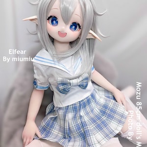 May include: A white doll with long silver hair, blue eyes, and a light blue and white plaid skirt. The doll is wearing a white sailor shirt with blue trim and a blue bow. The doll is sitting on a white fluffy surface. The text "Elfear By miumiu" is in the top left corner of the image. The text "Mozu 85cm doll's Master Photo By" is in the bottom right corner of the image.