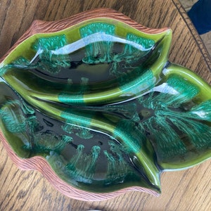 May include: A green and brown ceramic leaf-shaped serving dish with three sections. The dish has a glossy finish and a textured rim.