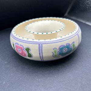 May include: A white ceramic ashtray with a floral design. The ashtray has a small inner bowl and a larger outer bowl. The flowers are pink, blue, green, and purple.