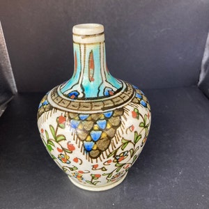 May include: A small, white ceramic vase with a rounded body and a narrow neck. The vase is decorated with a colorful floral pattern in shades of blue, green, red, and gold.