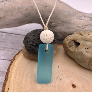 Op de afbeelding: Een lichtblauwe glazen hanger met een witte lavasteenkraal aan een wit koord.