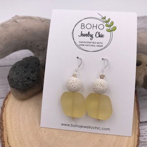 May include: A pair of yellow glass and white lava rock earrings with silver hooks. The earrings are handcrafted with 100% natural hemp. "BOHO Jewelry Chic" is printed on the card behind the earrings.