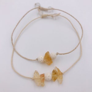 Könnte beinhalten: Zwei Armbänder aus natürlichen Materialien. Jedes Armband hat ein Schnurband und ist mit kleinen Stücken gelbem Citrin und weißen Lavasteinen verziert.