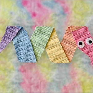 Może przedstawiać: Ręcznie robiony, kolorowy robak z włóczki z dużymi oczami. Robak jest wykonany z różnych kolorów włóczki, w tym fioletowej, niebieskiej, zielonej, żółtej i różowej.