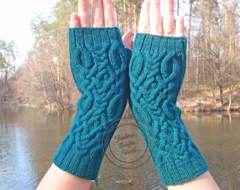 May include: Teal blue fingerless gloves with a cable knit pattern. The gloves are held up in front of a lake and trees.