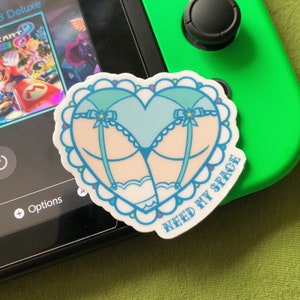 May include: A heart-shaped sticker with a blue and white lingerie design and the text "NEED MY SPACE".