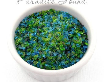 May include: A white bowl filled with small pieces of turquoise and green glass. The glass pieces are irregular in shape and size. The bowl is sitting on a white surface. The text "Paradise Found" is written in cursive above the bowl. The text "by Glass Diversions" is written below the bowl.