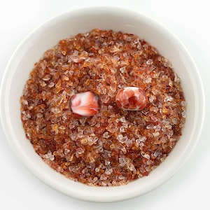May include: A white bowl filled with small, clear and brown glass pieces. Two red and white glass beads are on top of the glass pieces.