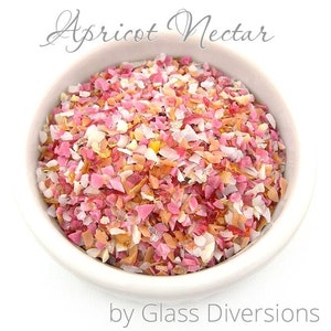Puede incluir: Un pequeño tazón blanco lleno de piezas de vidrio de colores en tonos rosa, naranja y blanco. Las piezas de vidrio son pequeñas e irregulares, parecidas a vidrio triturado o confeti. El texto "Apricot Nectar by Glass Diversions" está impreso debajo del tazón.
