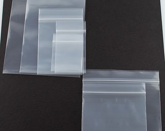 Könnte beinhalten: Sortiment von durchsichtigen Plastikbeuteln mit Reißverschluss in verschiedenen Größen. Die Beutel sind in einer Reihe auf einem schwarzen Hintergrund angeordnet.