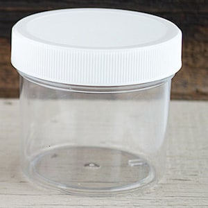 May include: A clear plastic jar with a white lid. The jar is empty and has a smooth, rounded bottom.