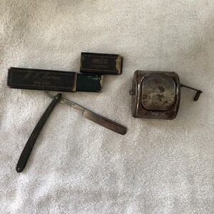 May include: An antique shaving set featuring a straight razor, two boxes of razor blades, and a small metal container. The razor is open, displaying the blade. The boxes have text that reads "S.F. Ferriere NEW YORK" and "HONELESS MADE IN FRANCE".
