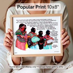 May include: A framed print, labeled "Popular Print 10x8", features a colorful illustration of women in traditional attire, some wearing black masks. The artwork includes Spanish text and is set in a light-colored wooden frame. The print measures 10 inches by 8 inches.