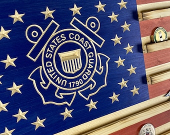 May include: A wooden American flag with a carved United States Coast Guard emblem in the center. The flag has slots for displaying medals or challenge coins.