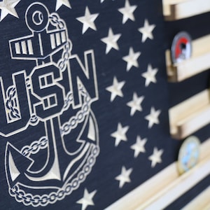 May include: A wooden US flag with a carved anchor and the letters USN. The flag has a wood grain finish and is designed to hold challenge coins.