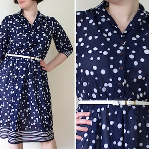 May include: A navy blue and white polka dot dress with a white belt and a button-up front. The dress has short sleeves and a slightly flared skirt.