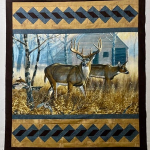 May include: A brown and tan quilt with a blue and brown diamond pattern border. The center of the quilt features a painting of a white-tailed deer buck and doe standing in a forest setting.