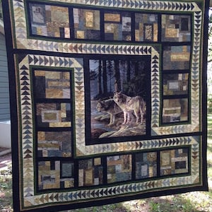 May include: A black and white quilt with a patchwork design. The center panel features a photo of two wolves in a forest setting. The quilt is bordered with a green and white geometric pattern.