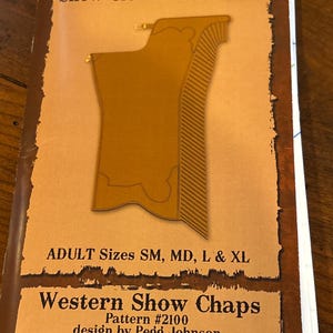 May include: A pattern book titled "Show Clothes Unlimited" featuring a design for Western Show Chaps. The cover displays a brown illustration of chaps, with text indicating adult sizes SM, MD, L & XL. The pattern is #2100, designed by Pegg Johnson.