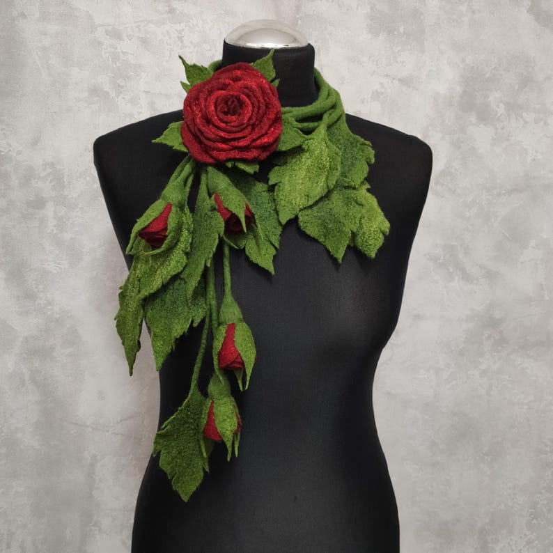 May include: A felt scarf with a red rose and green leaves. The scarf is draped over a black mannequin.