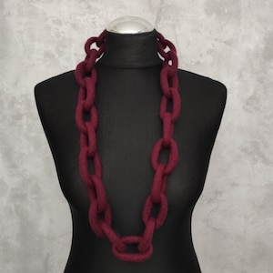 Puede incluir: Un collar de cadena burdeos exhibido en un maniquí negro. El collar está hecho de eslabones grandes y ovalados, creando un aspecto grueso y audaz. El color es un tono profundo y rico de rojo-púrpura, de unos 60 cm de largo.