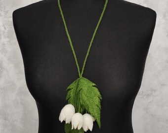 May include: A white felt flower necklace with green leaves. The necklace is made of felt and is a delicate and feminine piece of jewelry.