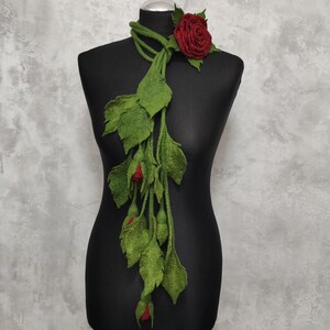 May include: A long green felt scarf with red felt roses. The scarf is draped over a black mannequin.