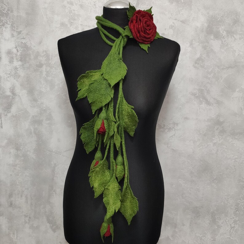 May include: A long green felt scarf with red felt roses. The scarf is draped over a black mannequin.