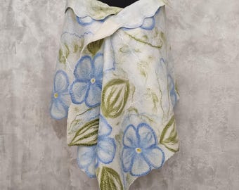 Könnte beinhalten: Ein weißer Schal mit blauen Blumen- und grünen Blattmustern. Der Schal ist auf einer schwarzen Schaufensterpuppe drapiert. Die Kanten des Schals haben ein gewelltes Design. Die Blumen haben gelbe Zentren.