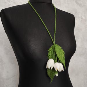 Pu&ograve; includere: Una collana di feltro verde con fiori di feltro bianco. I fiori hanno la forma di campane e sono raggruppati nella parte inferiore della collana.