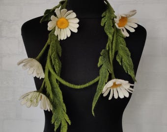 May include: A handcrafted daisy necklace made of felt, displayed on a black mannequin. The necklace features white daisy flowers with yellow centers and green leaves and stems. The floral design is a unique accessory.