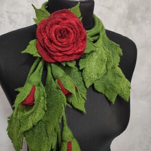 May include: A red felt rose with green felt leaves, forming a scarf or necklace. The rose is large and the leaves are long and flowing.