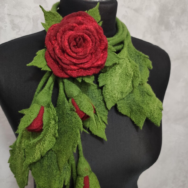 May include: A red felt rose with green felt leaves, forming a scarf or necklace. The rose is large and the leaves are long and flowing.