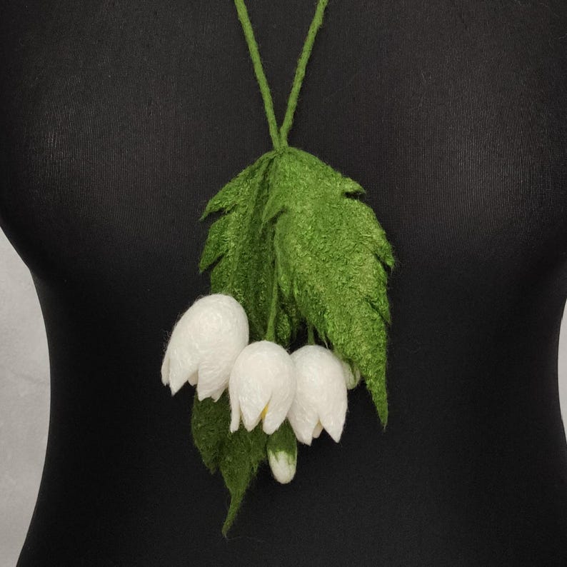 Pu&ograve; includere: Una collana di fiori in feltro bianco con foglie in feltro verde. I fiori sono raggruppati e assomigliano al mughetto.