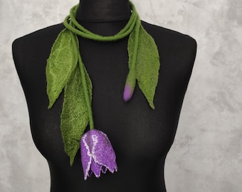May include: A felted scarf in the shape of a tulip, displayed on a black mannequin. The scarf features a purple flower with white accents, green leaves, and a green stem. The scarf is designed to be worn around the neck.