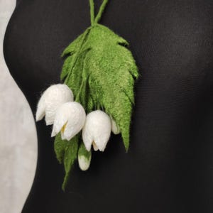 Pu&ograve; includere: Una collana di fiori di feltro bianco con foglie di feltro verde. I fiori hanno la forma del mughetto.