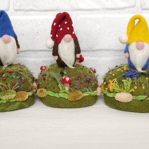 Puede incluir: Cinco peque&ntilde;as figuras de gnomos con barbas blancas y sombreros puntiagudos en verde lima, azul, rojo con puntos blancos, amarillo y naranja. Cada gnomo se apoya sobre una base redonda de color verde musgo decorada con flores bordadas, cuentas y tela.