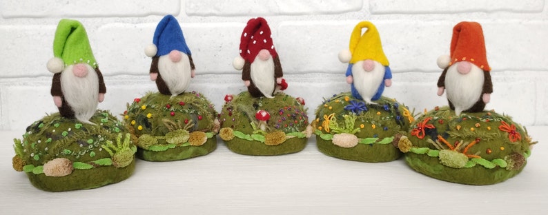 Puede incluir: Cinco peque&ntilde;as figuras de gnomos con barbas blancas y sombreros puntiagudos en verde lima, azul, rojo con puntos blancos, amarillo y naranja. Cada gnomo se apoya sobre una base redonda de color verde musgo decorada con flores bordadas, cuentas y tela.