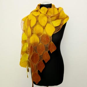 May include: A felted scarf featuring a gradient of circular shapes transitioning from bright yellow to deep orange. The scarf is constructed with a sheer, open-weave mesh base that connects the individual felted circles, creating a textured, layered appearance that drapes over the shoulders.